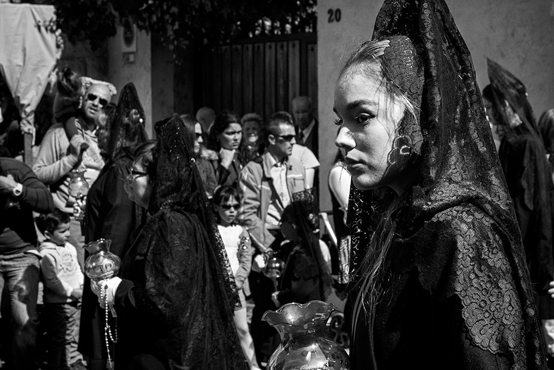 Una mujer con mantilla lleva un cirio entre una multitud.